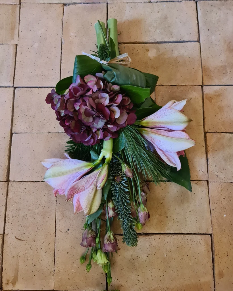 Bårebuket med lyserød amaryllis, mørk hortensia og vintergrønt som en smuk sidste hilsen ved begravelse eller bisættelse.