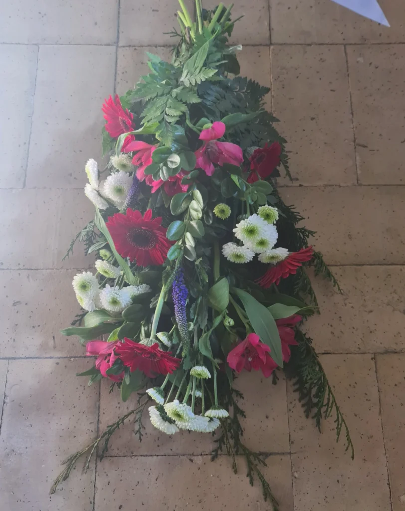 Bårebuket med røde gerbera, pink alstroemeria og hvide blomster som en smuk sidste hilsen ved begravelse eller bisættelse.
