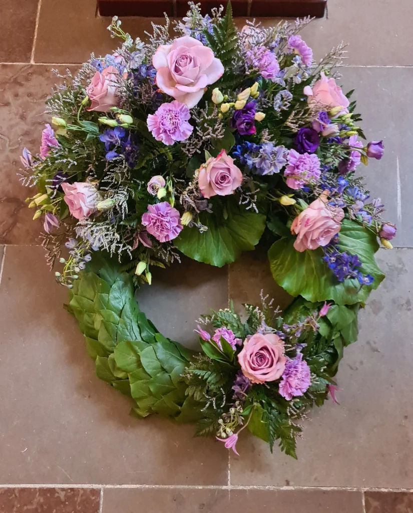 Krans til begravelse med lyserøde roser, lilla nelliker, lisianthus og blå ridderspore.